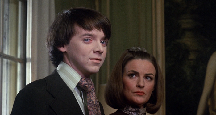 Boy smiling mischievously at the camera, while his mother frowns at him