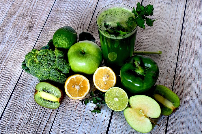 A delicious green smoothie on a table with green vegetables & fruits