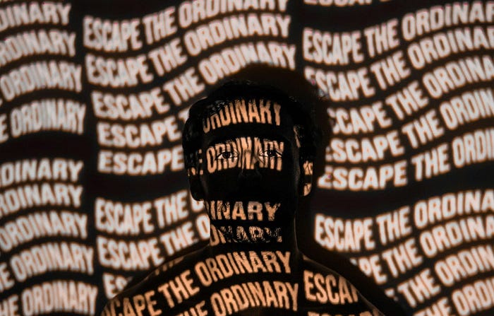 man standing with projector displaying “escape the ordinary” covering his face.