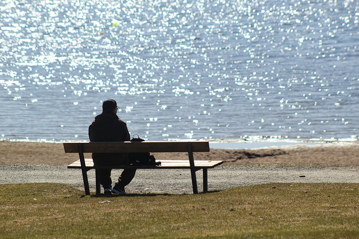person getting rest on a bench beside sunny waters.