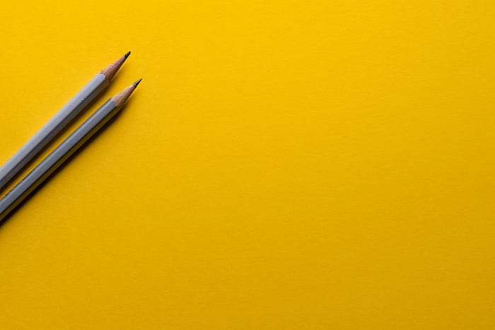 Two graphite pencils on a vibrant yellow background, symbolizing creative design and idea generation.
