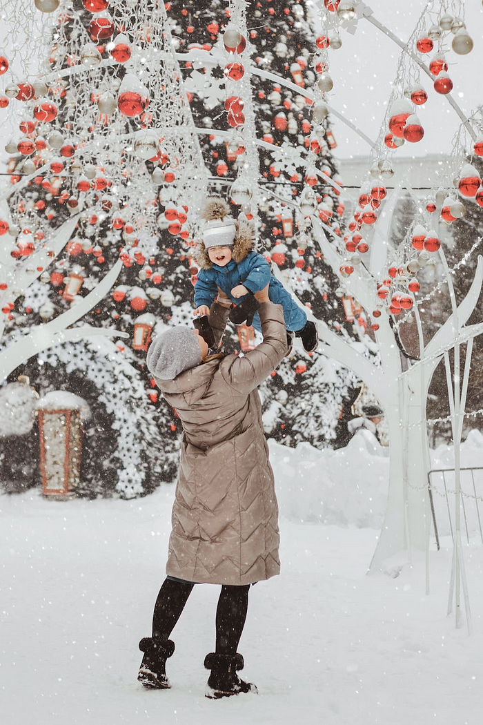 A mom is holding up her toddler in the snow in a playful way.