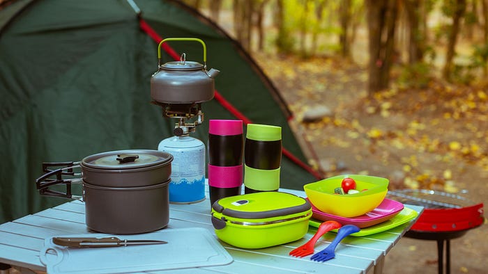 Table with camping gear including tea pot on burner and dishware