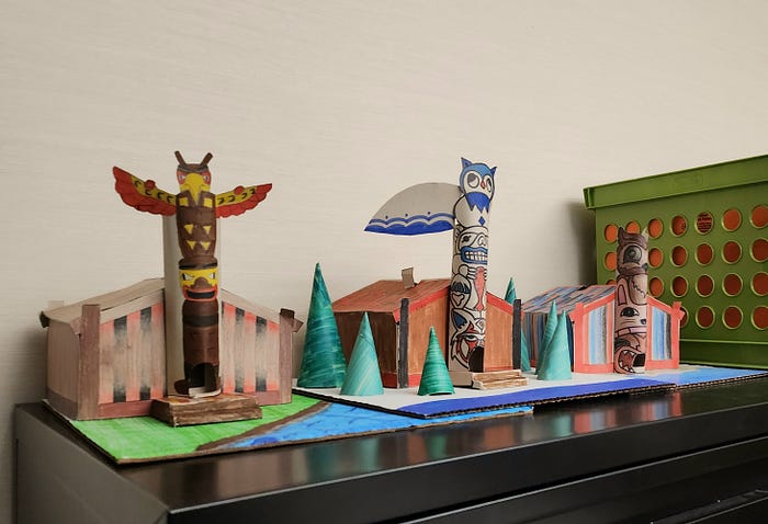 Three small, colorful houses with large poles featuring animals on them at the front.
