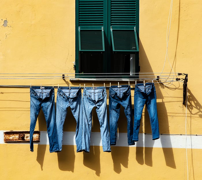 A row of denim jeans hanging to dry under a window and against a yellow wall.