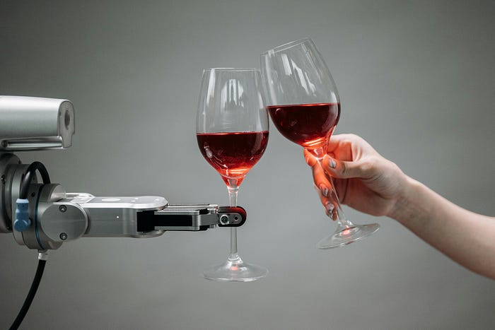A robotic arm holds a wine glass and toasts it with another human hand holding a wine glass.