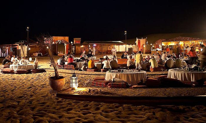 Desert camp dinner experience with tourists under Dubai travel packages.