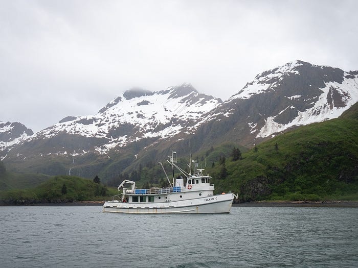 Research vessel Island C in cove with snow covered mountains in the background.