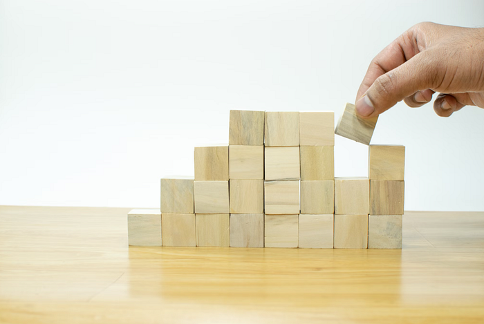 Hand arranging wood block stacking as step stair on wooden table