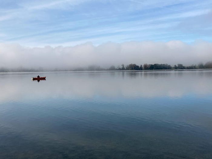 Lake with solitary fisherman in boat — is climate an existential crisis?