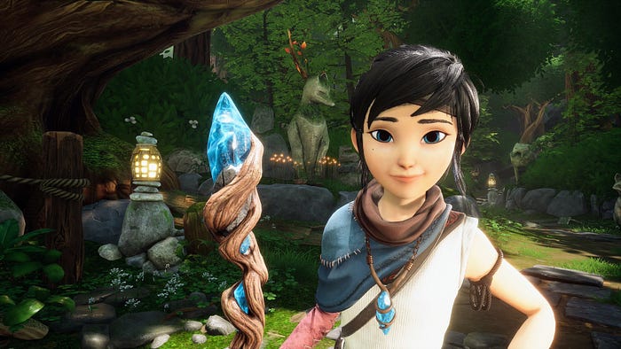 Kena, the protagonist of Kena: Bridge of Spirits, poses for the camera while smiling and holding her magical staff. The staff is topped with a blue crystal, and a lush green forest path unfolds behind her.