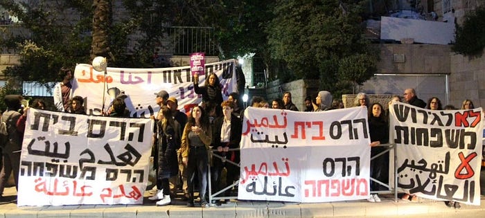People holding signs against home demolition, in Hebrew and Arabic