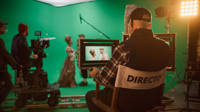 Film set with a director and two cameramen visible, filming a couple in period costumes against a large green screen