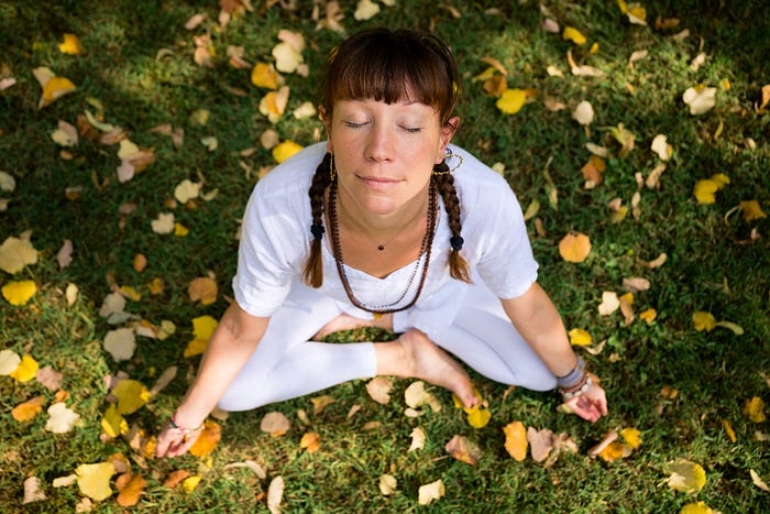 Woman with braided hair sitting crossed legged on the grass in autumn and looking very calm.