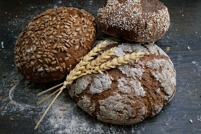 Three round loaves of bread and a wheat stalk. Photo courtesy of Wesual Click and Unsplash.