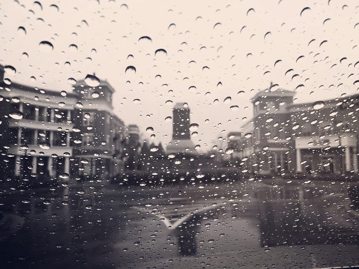 Black and white image of buildings taken through a rainy windshield.