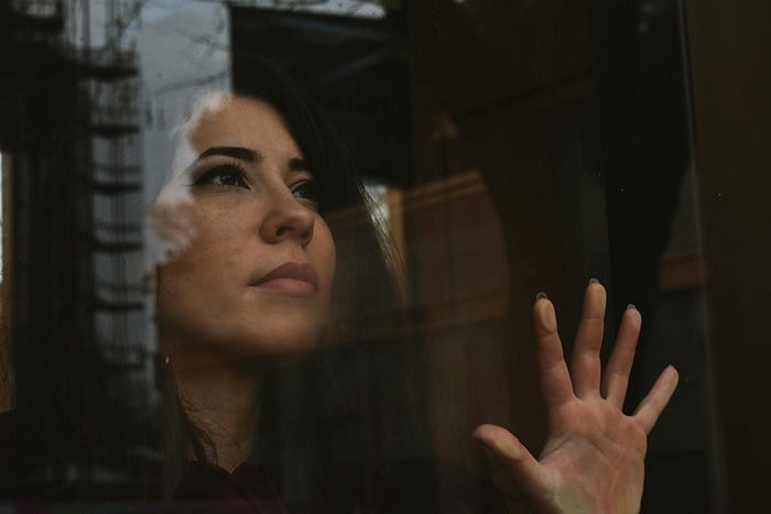 A woman standing by a window touching the glass