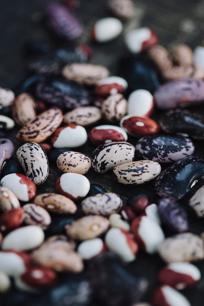 An assortment of seeds on a wooden table: beans mottled in shades of burgundy, beige, white and black