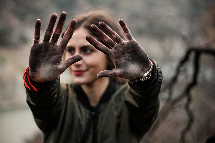 A woman displaying her dirt-covered hands prominently, illustrating “getting your hands dirty” as a designer.