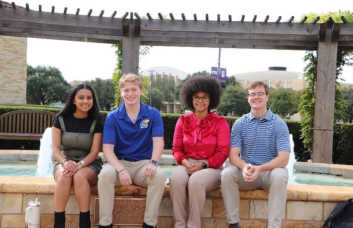 Students sit on the ledge of a fountain.