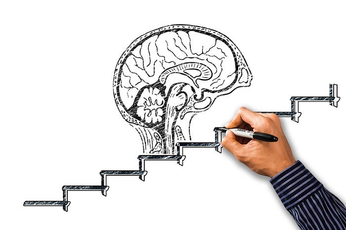 A disembodied hand uses a black marker to draw a brain on a set of stairs