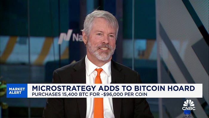 Michael Saylor in a business suit is interviewed on CNBC with an on-screen banner reading “MicroStrategy Adds to Bitcoin Hoard — Purchases 15,400 BTC for ~$96,000 per coin,” during a Market Alert segment.