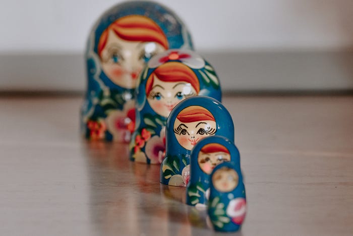 A series of five blue, wooden, Russian matryioshka dolls in a slightly angled vertical row, each smaller than the one behind it