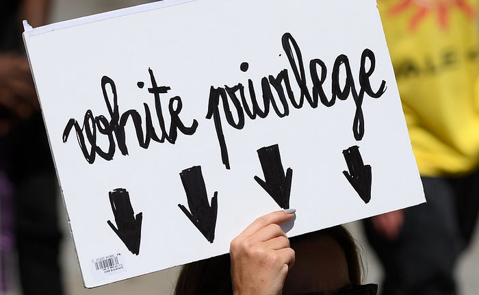 A woman holding up a sign reading “White privilege” with arrows pointing downward.