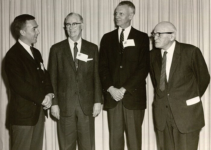 A black and white photo of four men stading and talking.