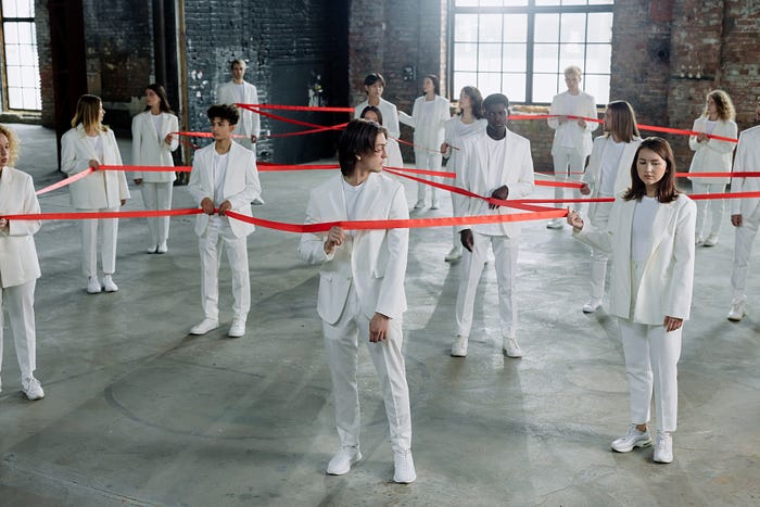 over a dozen people all wearing white suits holding a long red ribbon