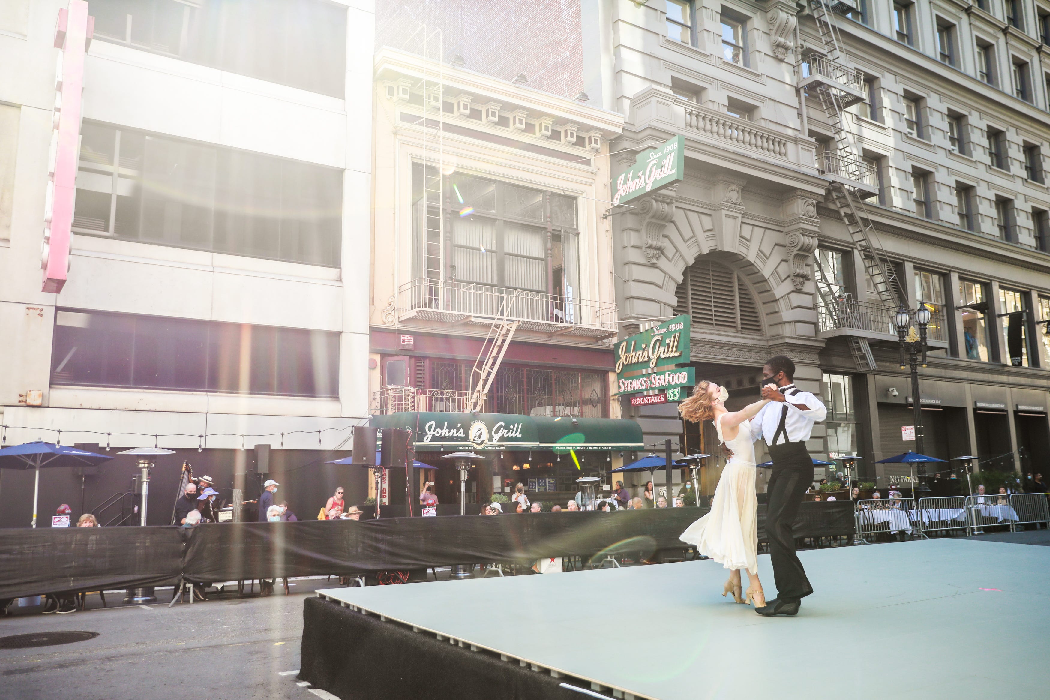 Two people wearing face masks dancing on a stage on a street.