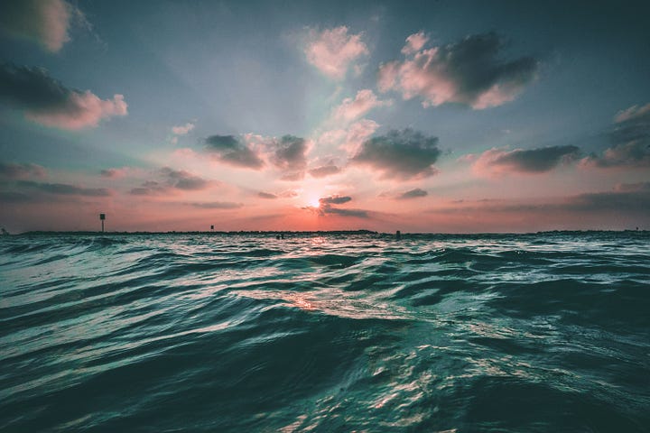 The sun setting over a calm ocean, with gentle waves lapping at the shore.