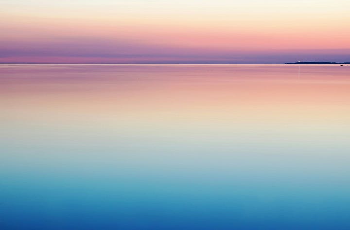 A person standing alone on a misty beach at sunrise, looking out at the calm ocean.