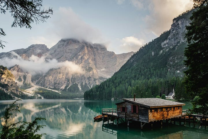 A single person sitting on a dock by a calm, misty lake at sunrise, engaged in quiet contemplation.