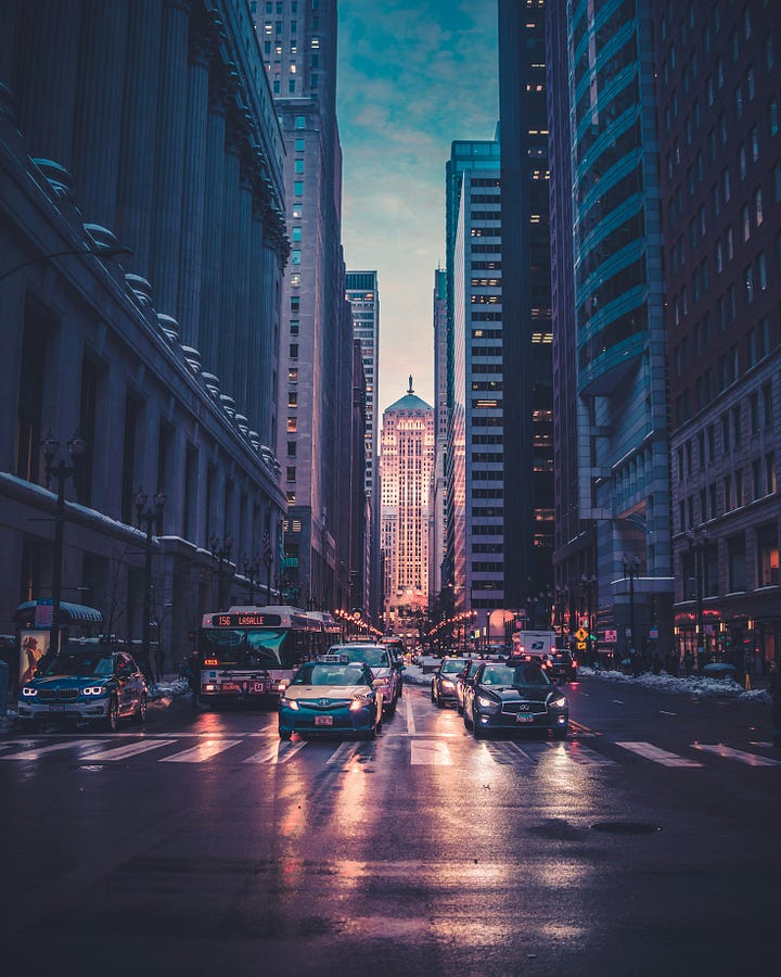 A wide, slightly blurred photograph of a crowded city intersection at night, conveying a sense of constant motion and anonymous connection.