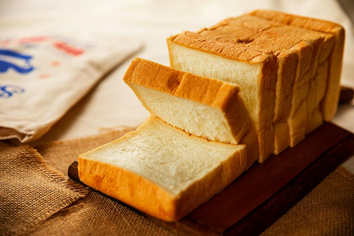 A single loaf of artisan bread sitting on a wooden cutting board, with a dramatic shadow.