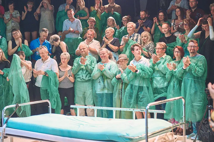 Stojąca owacja na zakońćzenie. Widownia ubrana w zielone szpitalne flizeliny.