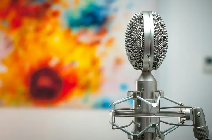 A close-up of a microphone positioned in front of a colorful, abstract painting with bright hues.