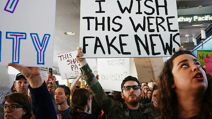 Photo of protesters with “I wish this were fake news” sign