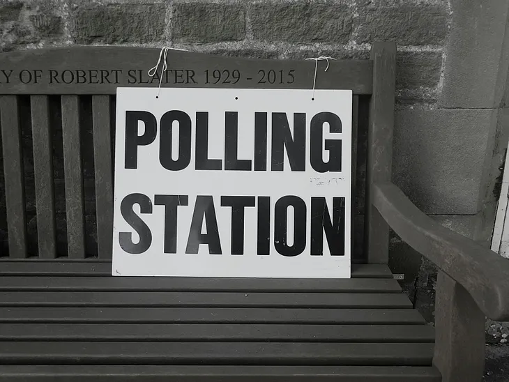 Memorial bench with a Polling Station sign tied to it.