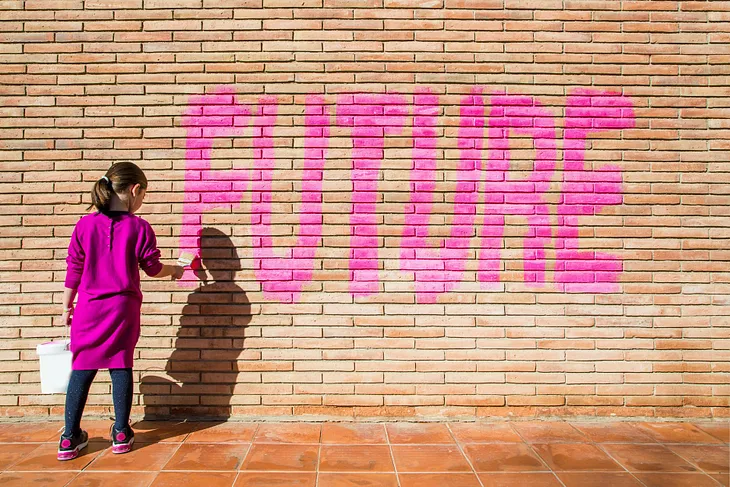 Young girl painting the word “Future” on a brick wall
