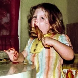Little girl eating a piece of chicken with gusto.