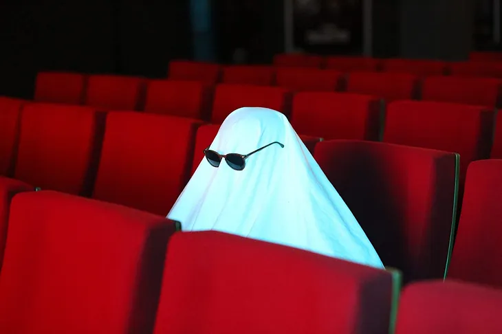 A ghost (white sheet over an object) with sunglasses in movie seats.