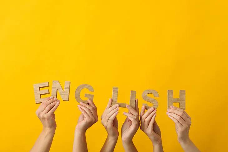 Hands holding up wooden letters spelling the word “English” against a yellow background