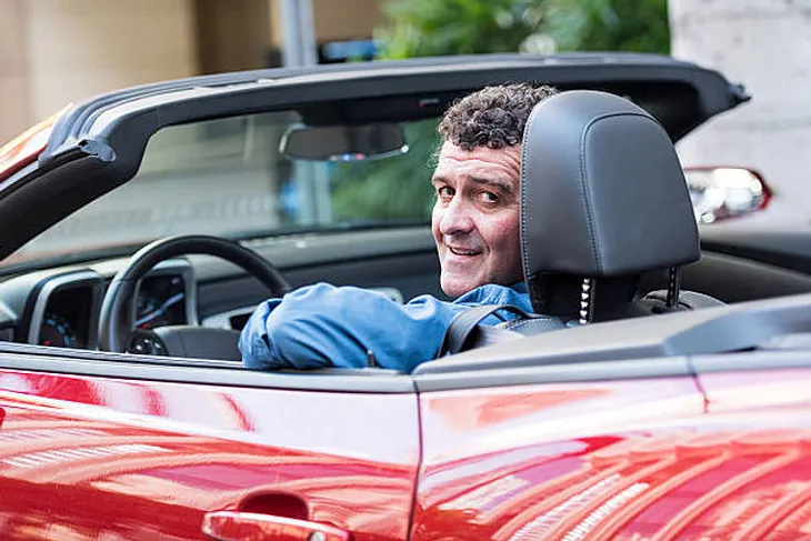 A middle-aged man sitting in a red convertible.