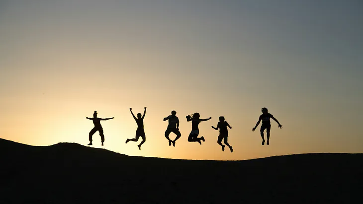 A sunset with six people jumping in the air. They might be friends.