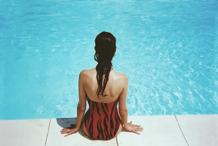 Photo of the back of a female sitting by a pool with wet hair