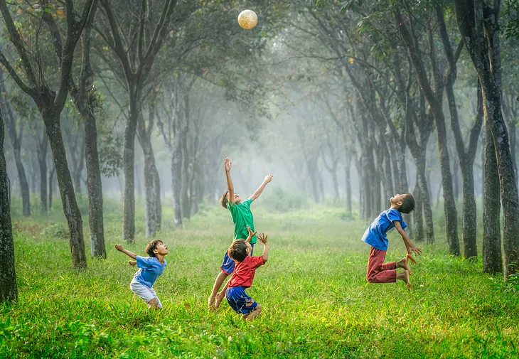 Four boys play with a football in a tree-lined meadow