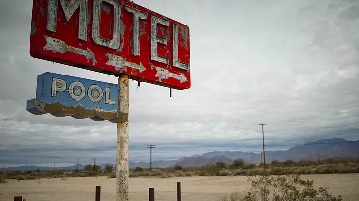 A decrepit sign in a desolate landscape says “Motel” & “pool”. Leah Welborn.