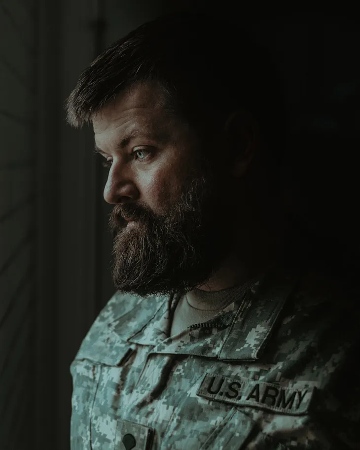 Gentleman with thick brownish beard and blue eyes, looking to the right (anatomical) staring off, lost in thought. He is wearing an US army uniform.